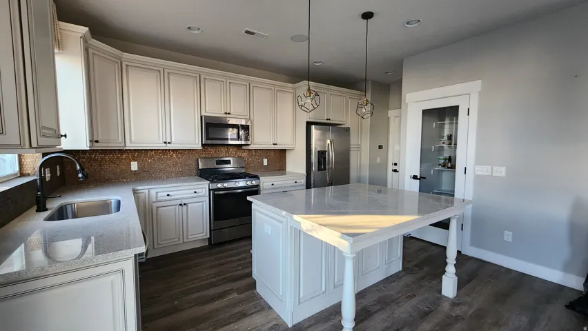Kitchen featuring stainless steel appliances, pendant lighting, light stone countertops, tasteful backsplash, and dark wood finished floors