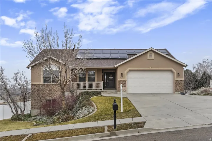 View of front of home featuring brick siding, a porch, stucco siding, concrete driveway, and roof mounted solar panels