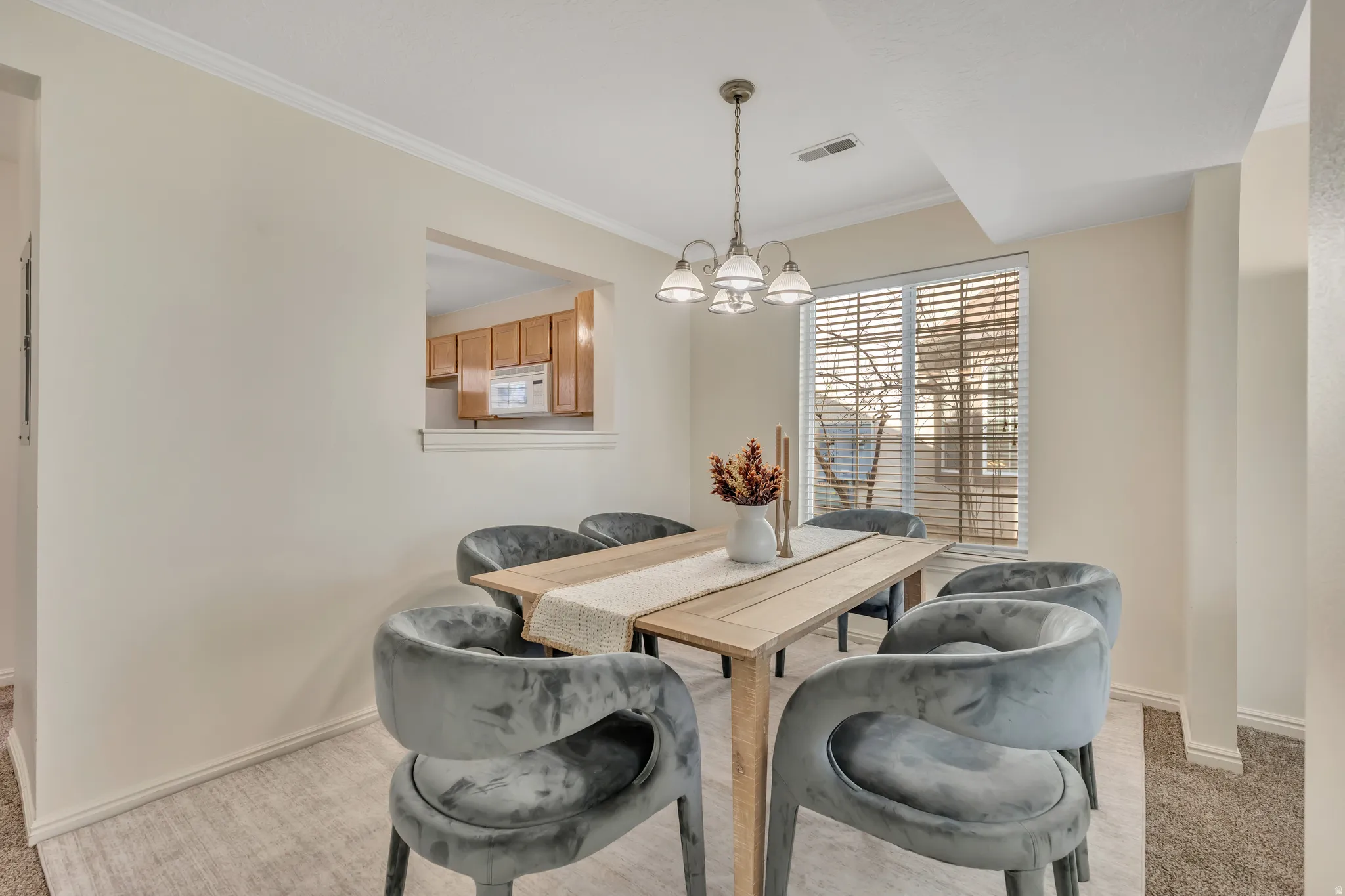 Dining space with light carpet, crown molding, and a chandelier