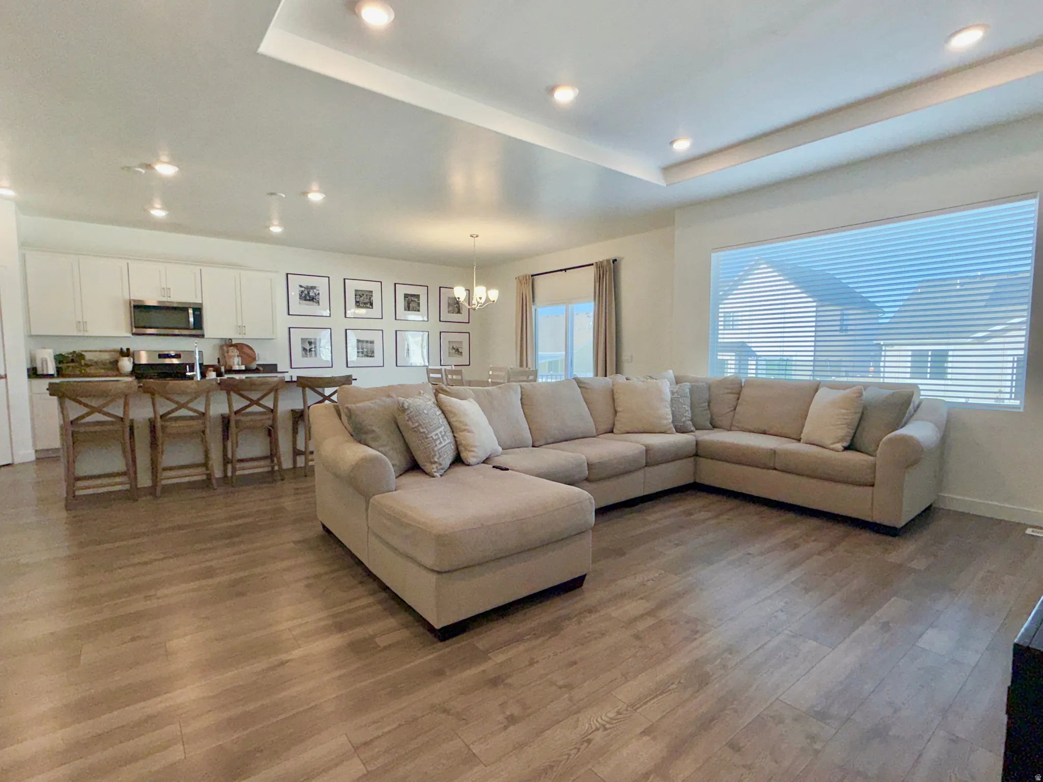 Living area with a chandelier, light wood finished floors, a raised ceiling, and recessed lighting