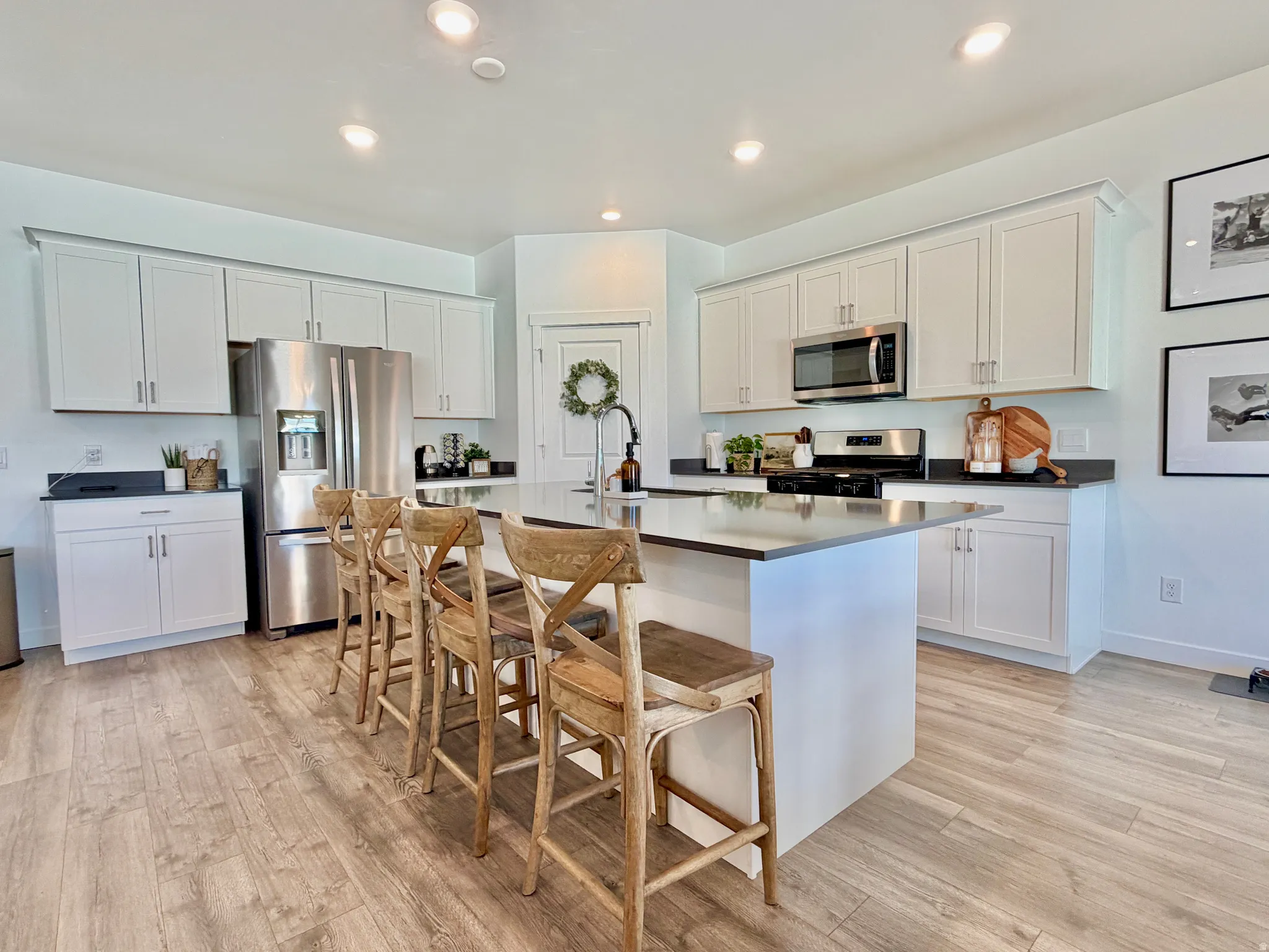 Kitchen featuring white cabinets, stainless steel appliances, a kitchen breakfast bar, light wood finished floors, and recessed lighting