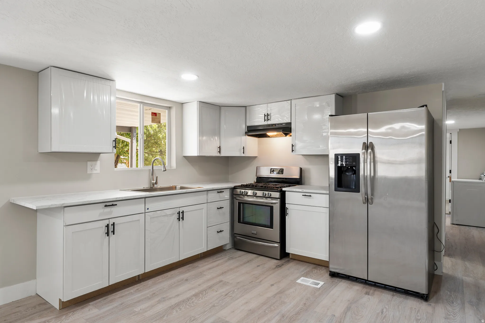 Kitchen with appliances with stainless steel finishes, light countertops, white cabinets, light wood-style flooring, and washer / clothes dryer