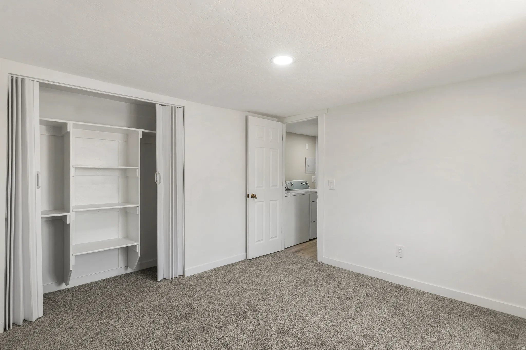 Unfurnished bedroom featuring light carpet, a textured ceiling, a closet, and washer and dryer