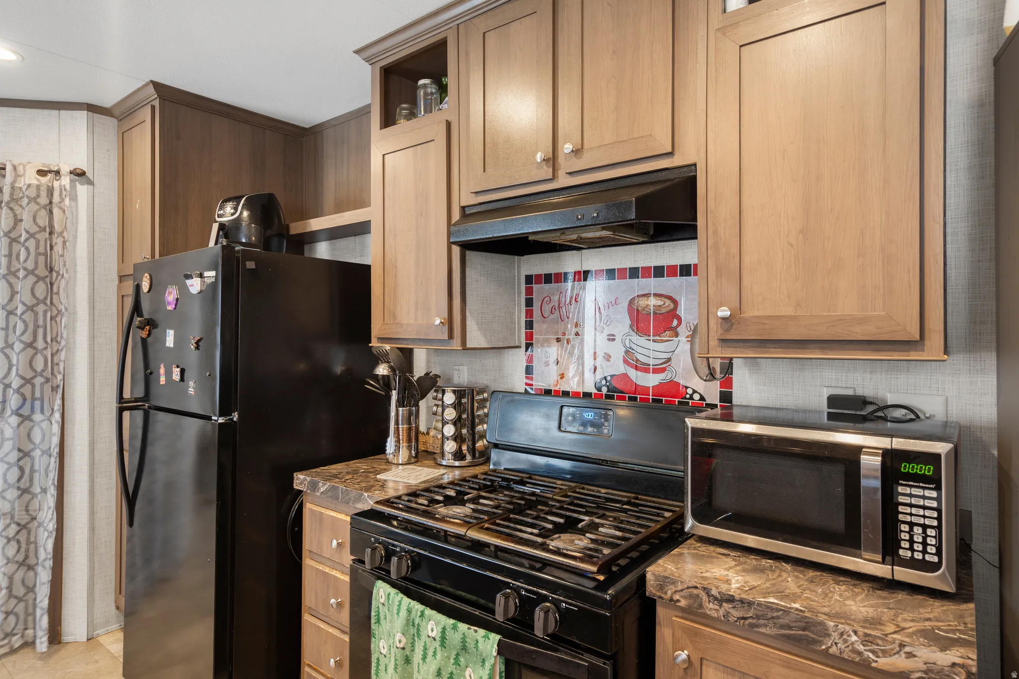 Kitchen with black appliances, under cabinet range hood, dark countertops, decorative backsplash, and open shelves