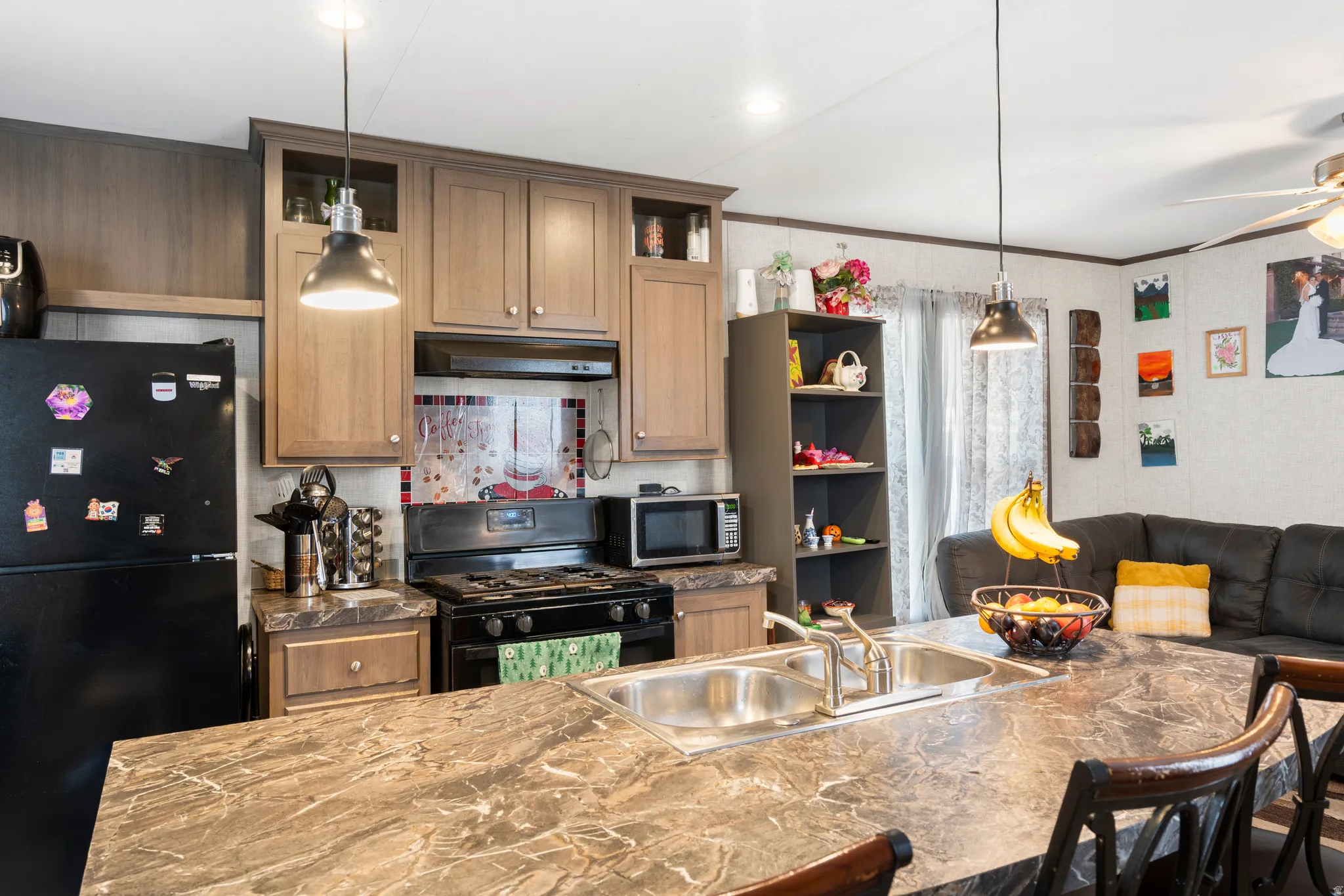 Kitchen featuring black appliances, pendant lighting, under cabinet range hood, crown molding, and tasteful backsplash
