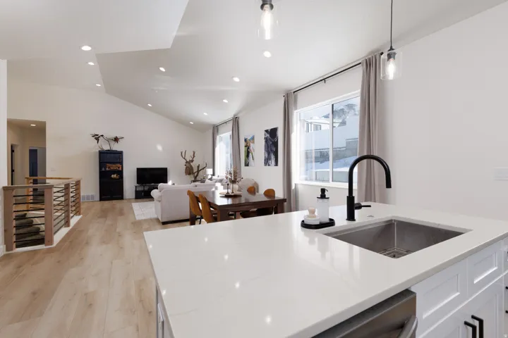 Kitchen with hanging light fixtures, recessed lighting, light wood-style flooring, light stone countertops, and vaulted ceiling