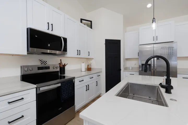 Kitchen featuring appliances with stainless steel finishes, white cabinetry, light stone countertops, decorative light fixtures, and recessed lighting