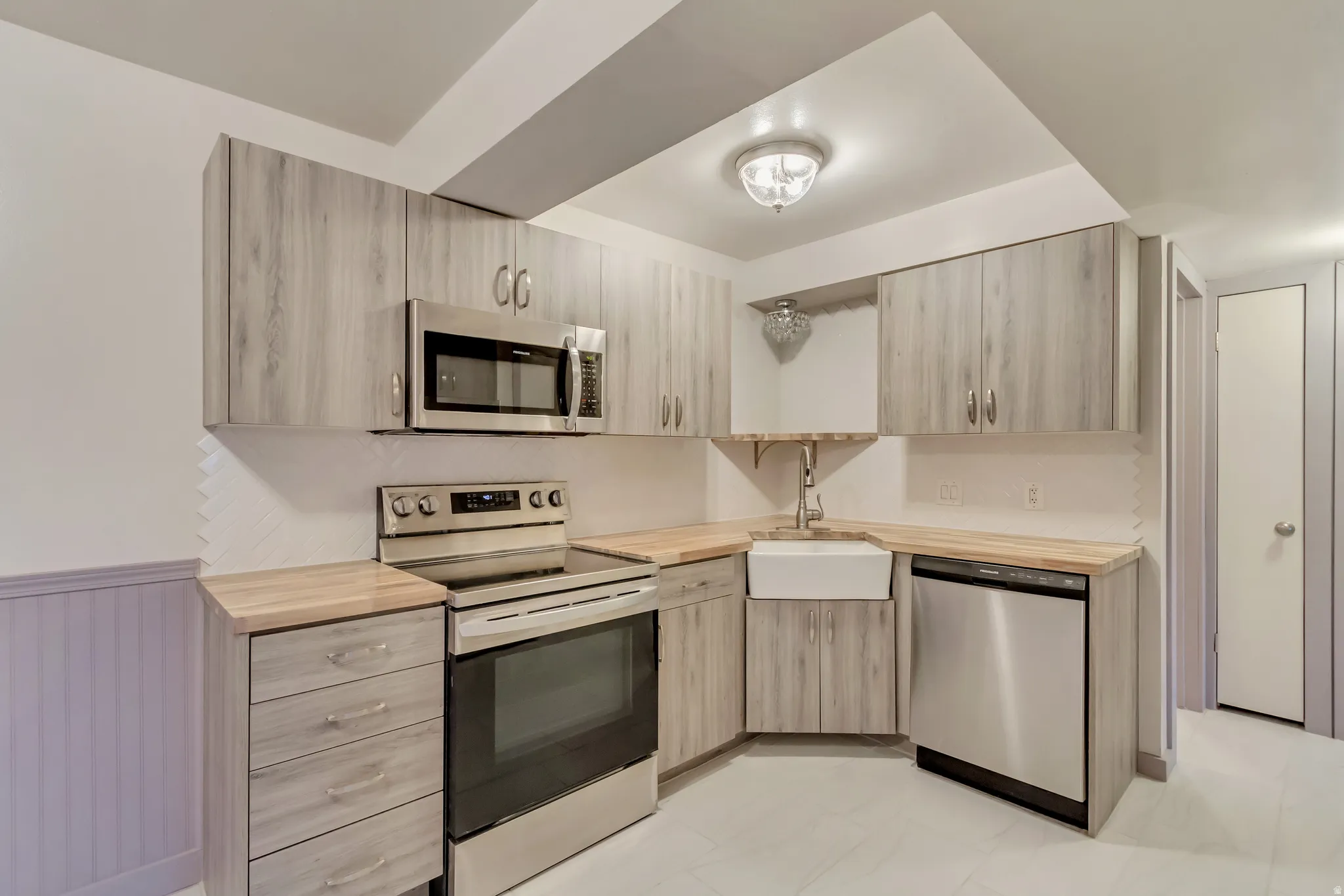 Kitchen featuring stainless steel appliances, light wood finish cabinetry, modern cabinets, and a wainscoted wall