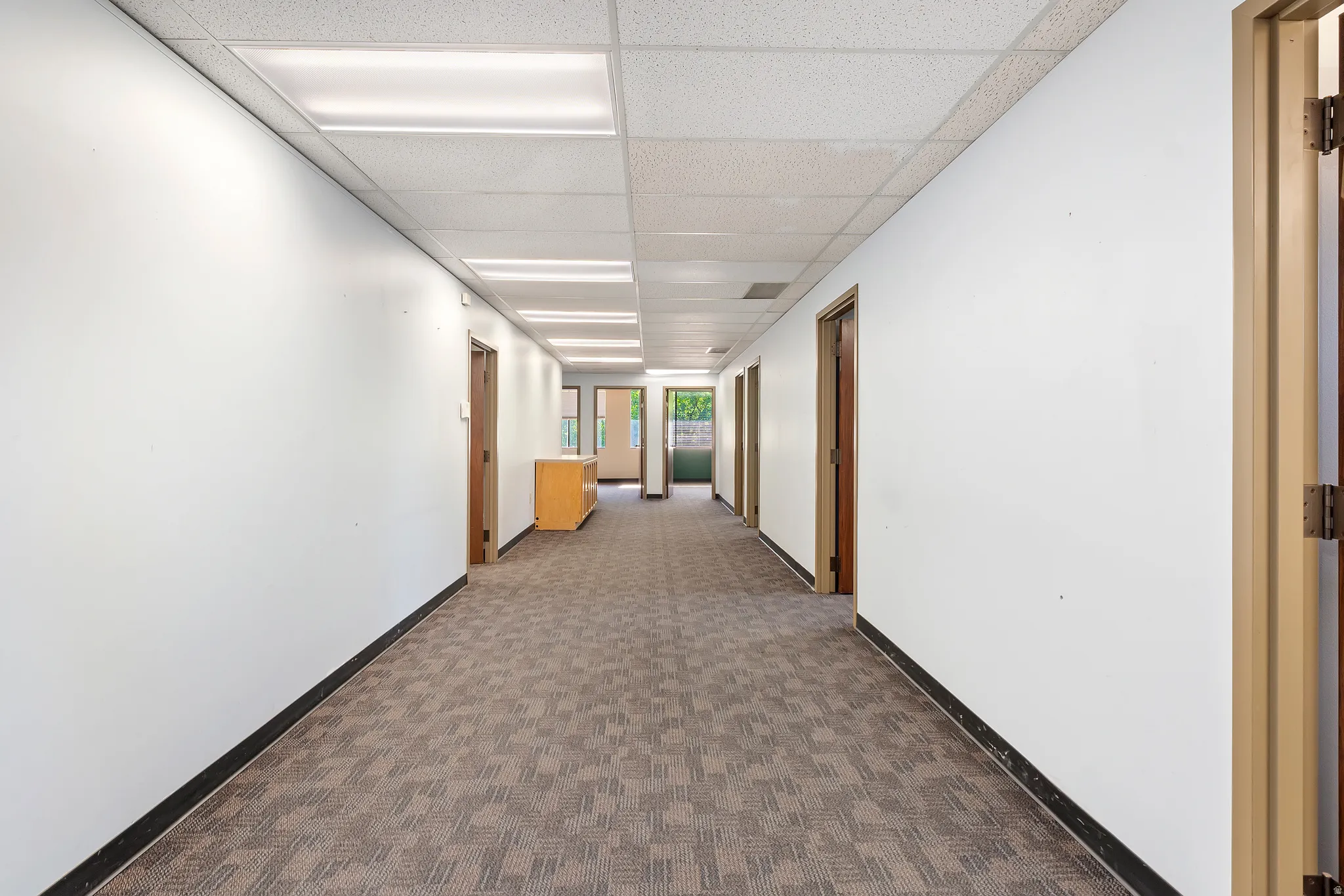 Hall featuring a paneled ceiling and dark carpet