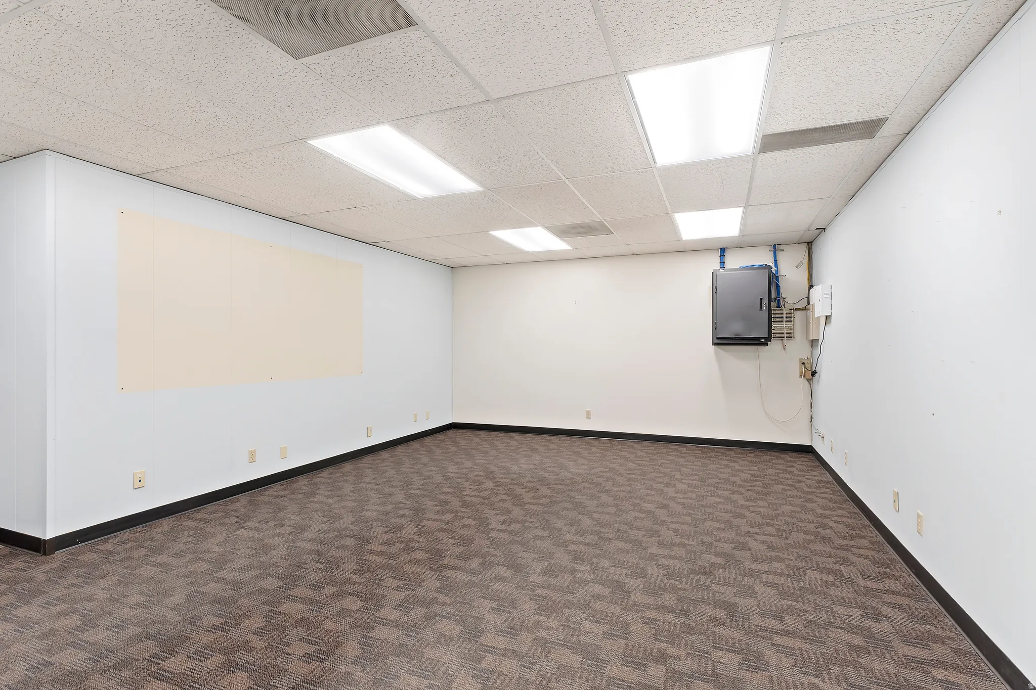 Empty room with dark carpet, a drop ceiling, and electric panel
