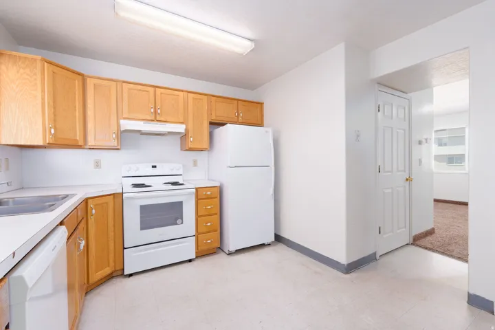 Kitchen featuring white appliances, light countertops, under cabinet range hood, and light floors