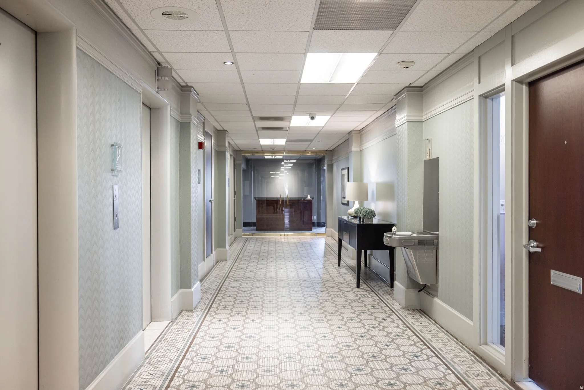Corridor featuring a paneled ceiling, light floors, elevator, and wallpapered walls