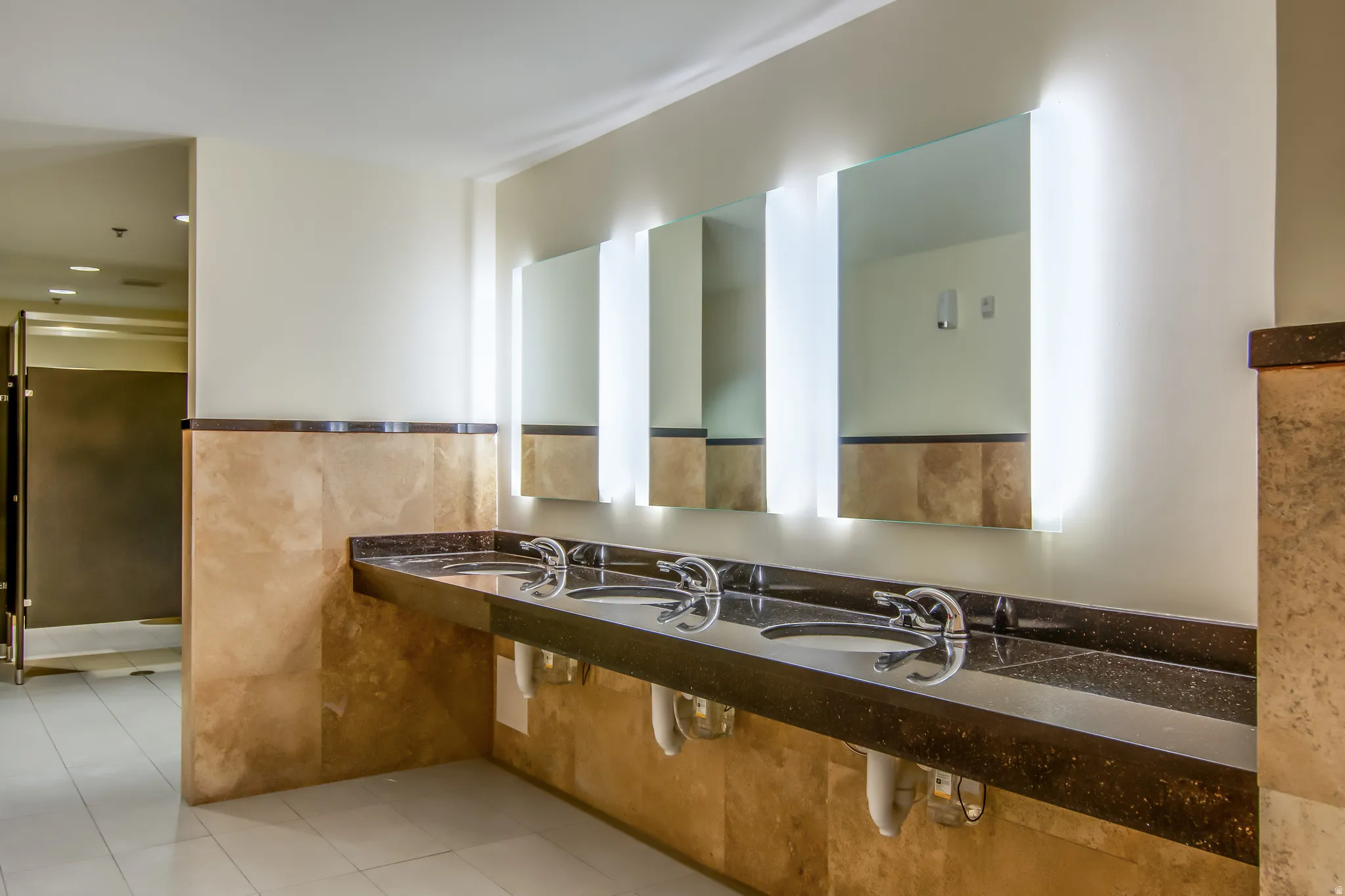 Bathroom featuring light tile patterned floors, double vanity, tile walls, recessed lighting, and wainscoting