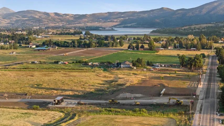 Expansive undeveloped land featuring a paved road frontage, visible construction activity, and distant water body