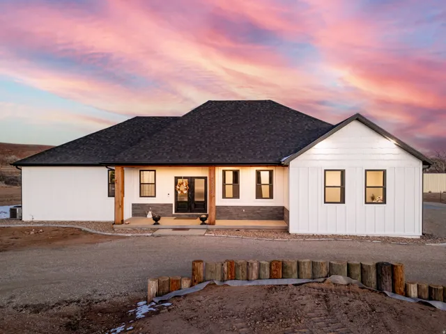 Back of property at dusk with a porch and a shingled roof