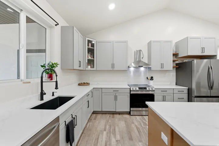 Kitchen featuring stainless steel appliances, light wood-style floors, light stone counters, wall chimney range hood, and gray cabinets