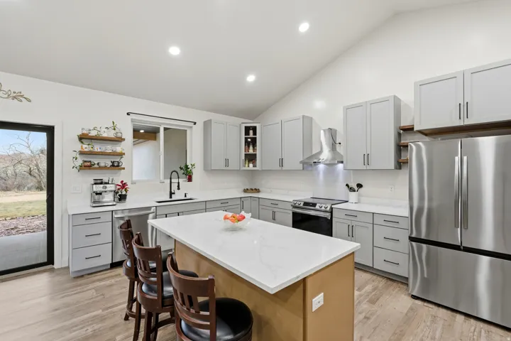 Kitchen featuring open shelves, stainless steel appliances, gray cabinetry, vaulted ceiling, and a kitchen island