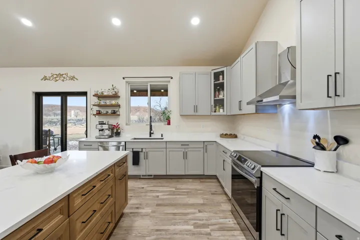 Kitchen with stainless steel appliances, wall chimney exhaust hood, gray cabinetry, light wood-style floors, and lofted ceiling