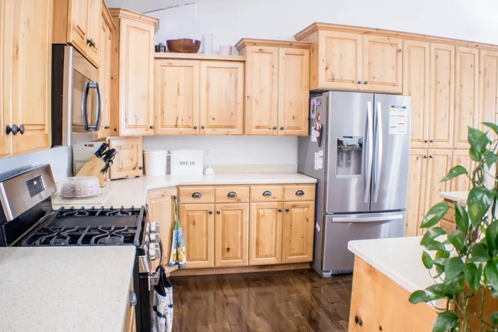 Kitchen with light brown cabinetry, appliances with stainless steel finishes, dark wood-style flooring, and light stone counters