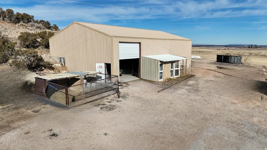 Large corrugated metal building with a white roll-up door, an attached small structure with multiple windows, and extensive gravel ground cover