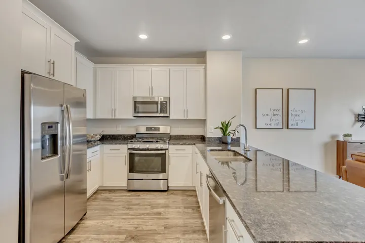 Kitchen with dark stone counters, appliances with stainless steel finishes, white cabinets, light wood-style flooring, and recessed lighting