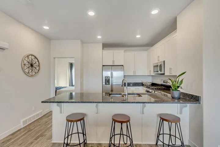Kitchen featuring white cabinets, a peninsula, appliances with stainless steel finishes, dark stone counters, and light wood-type flooring