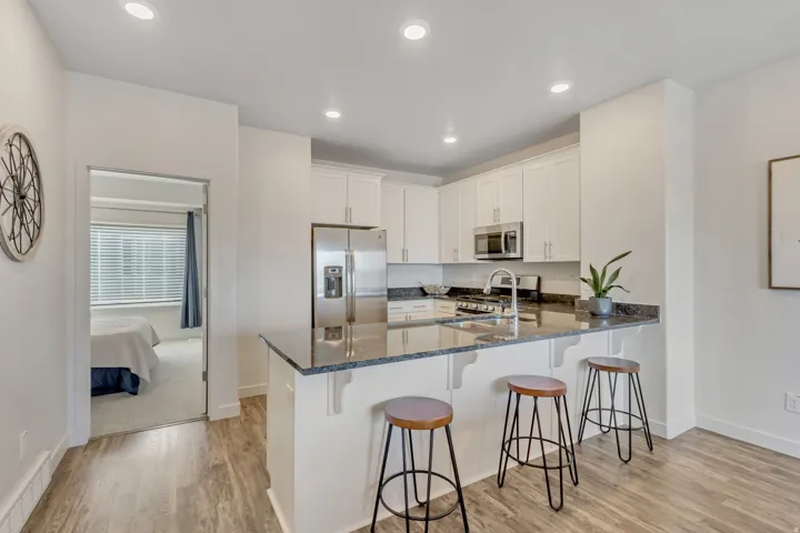 Kitchen with dark stone countertops, stainless steel appliances, white cabinets, a peninsula, and light wood-type flooring