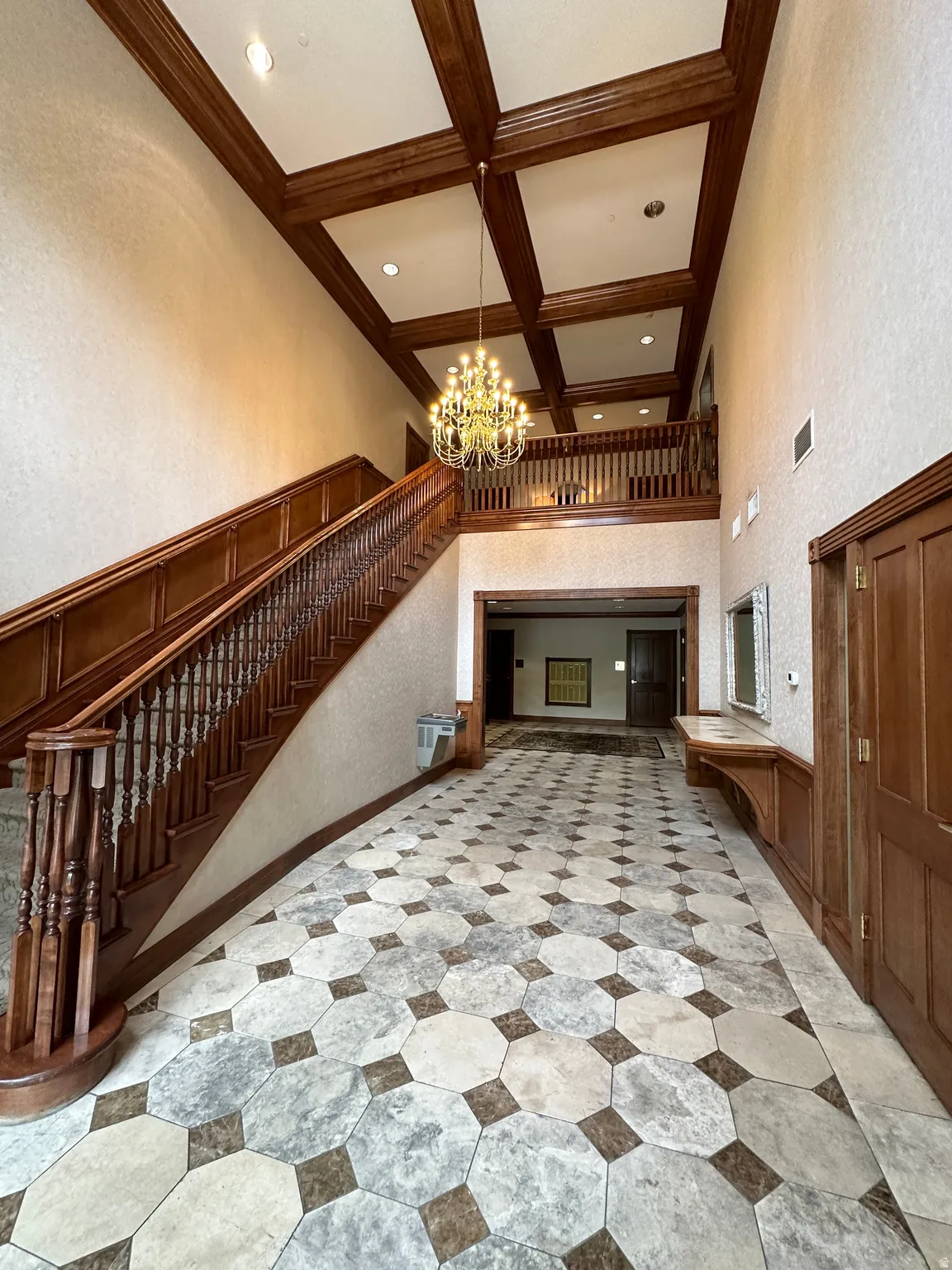 Unfurnished living room featuring stairs, coffered ceiling, a towering ceiling, a chandelier, and beamed ceiling