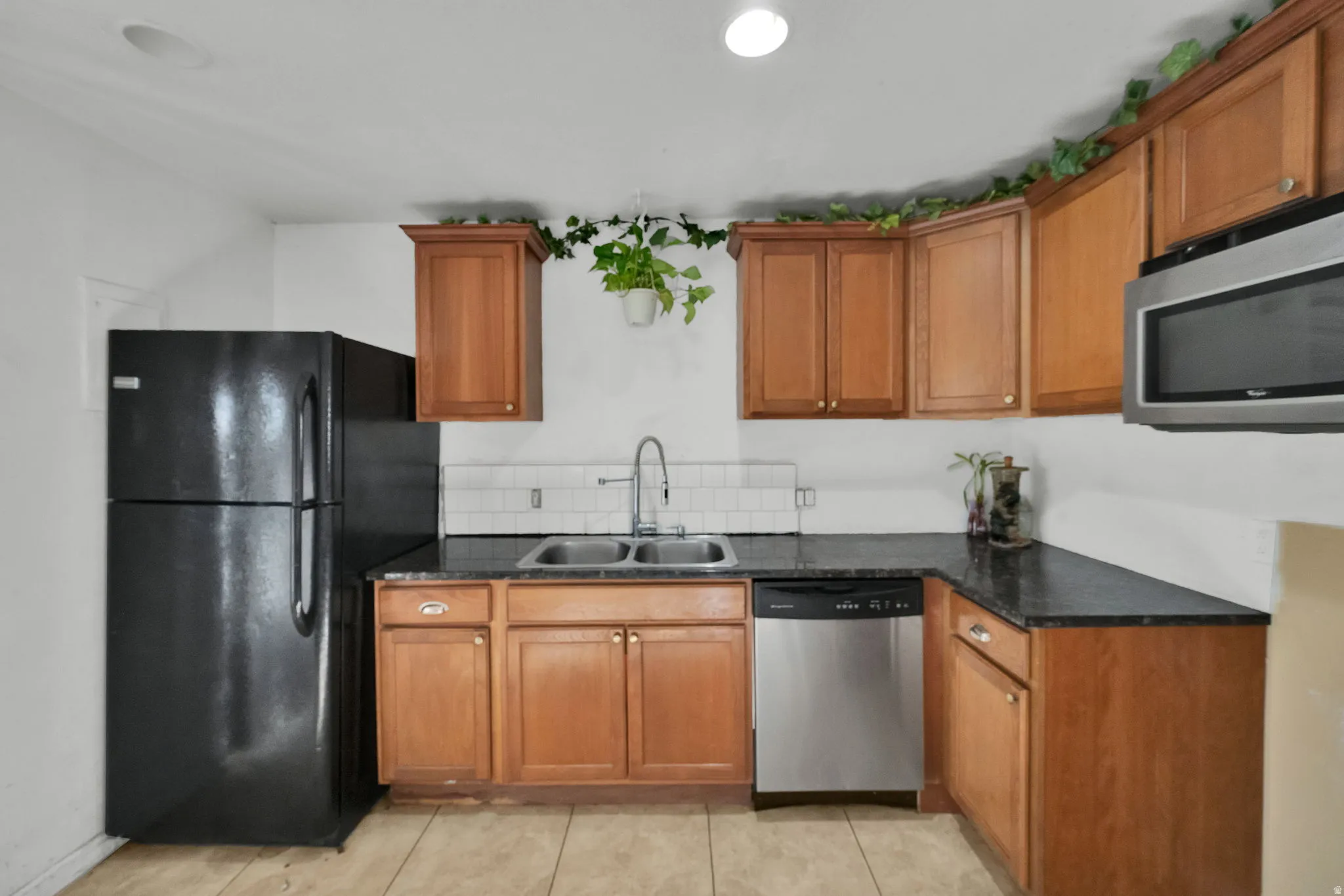 Kitchen with brown cabinetry, appliances with stainless steel finishes, light tile patterned floors, recessed lighting, and backsplash