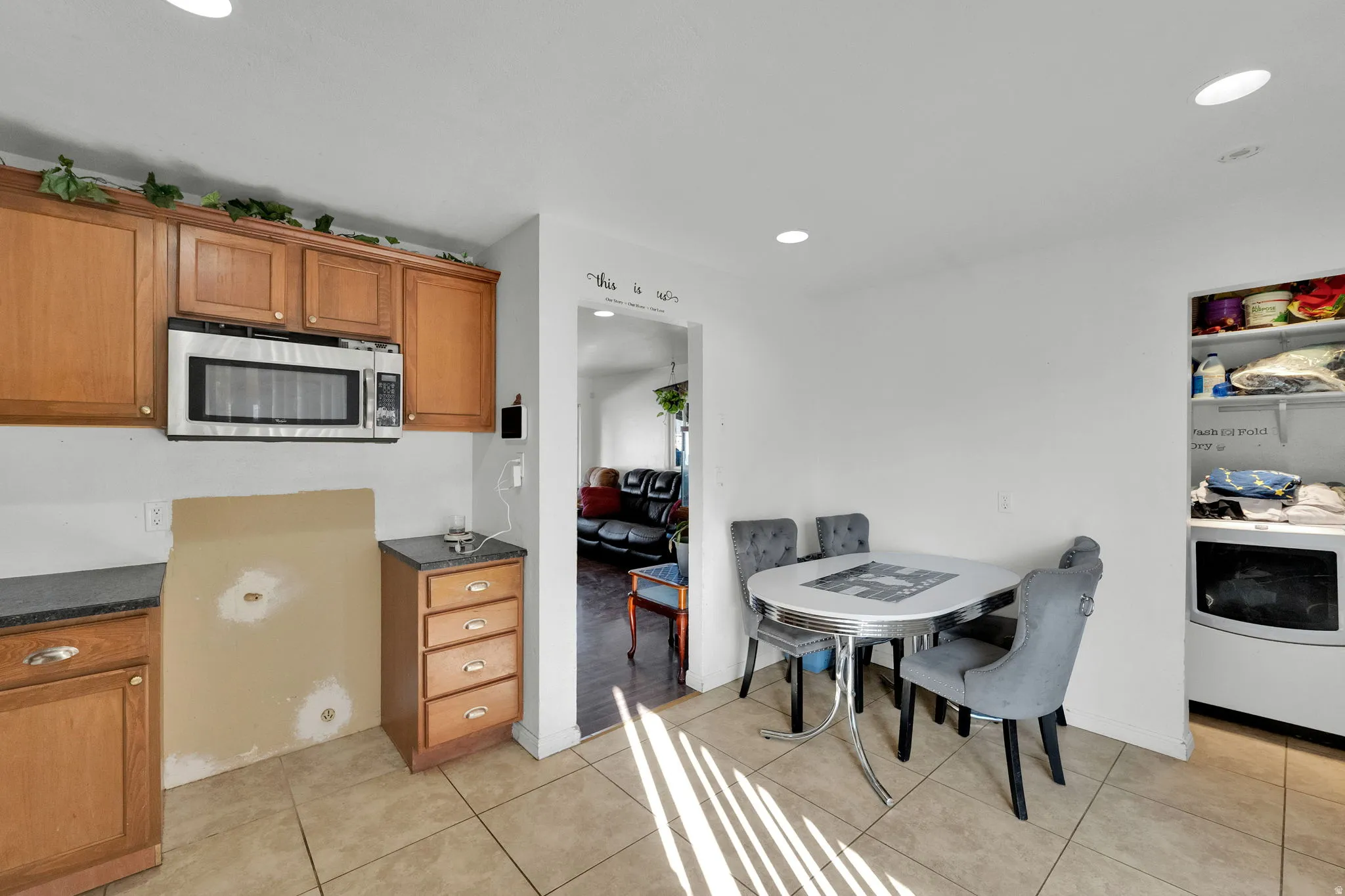 Kitchen featuring brown cabinetry, washer / dryer, stainless steel microwave, recessed lighting, and light tile patterned floors