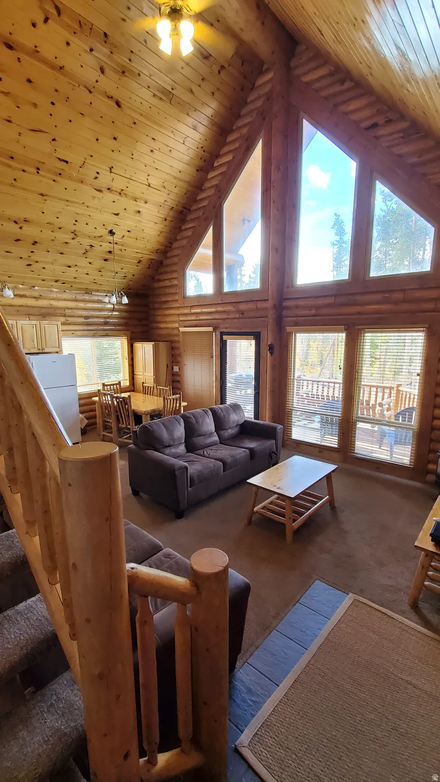 Carpeted living area featuring wooden ceiling, rustic walls, high vaulted ceiling, a ceiling fan, and stairway