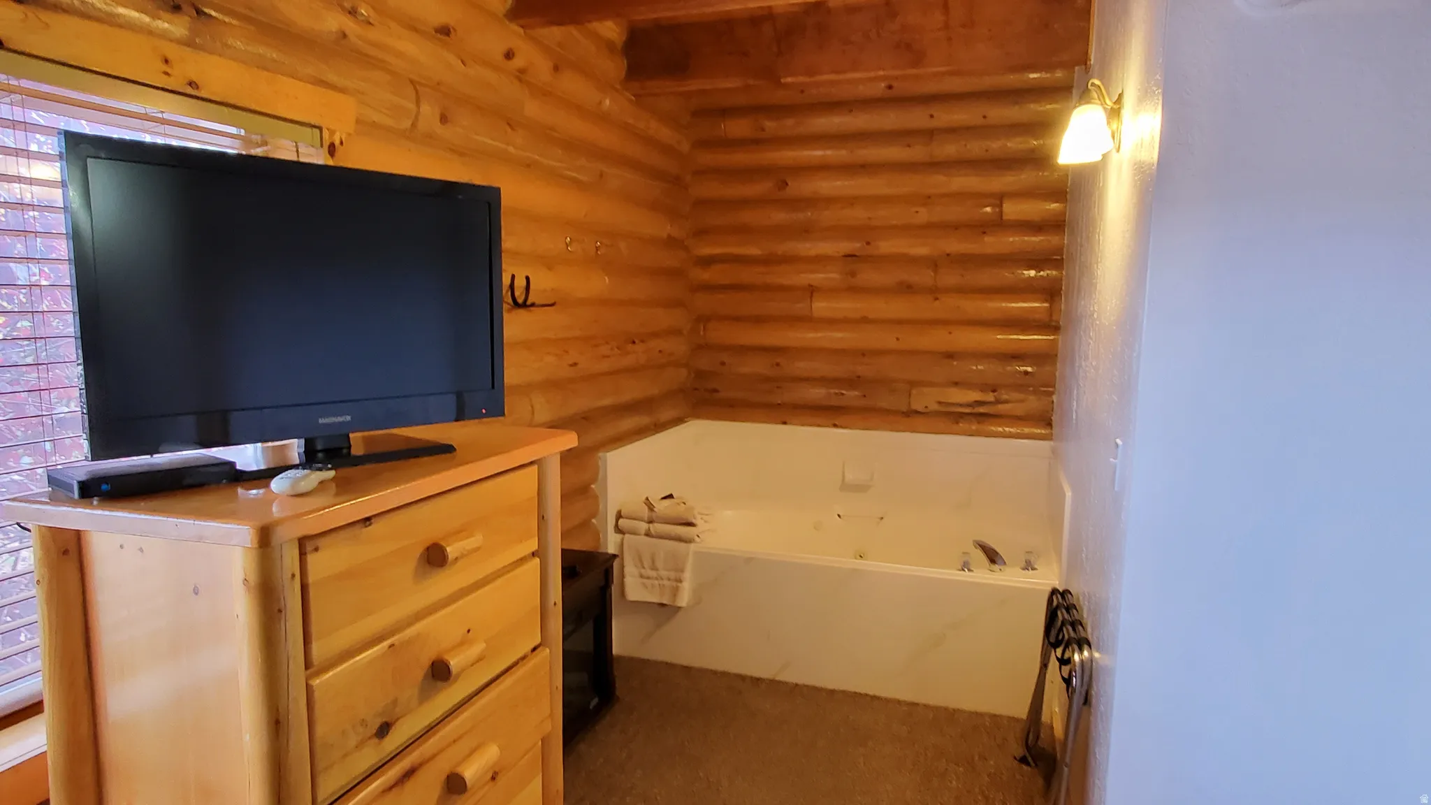 Bathroom featuring a garden tub, log walls, light colored carpet, and vanity