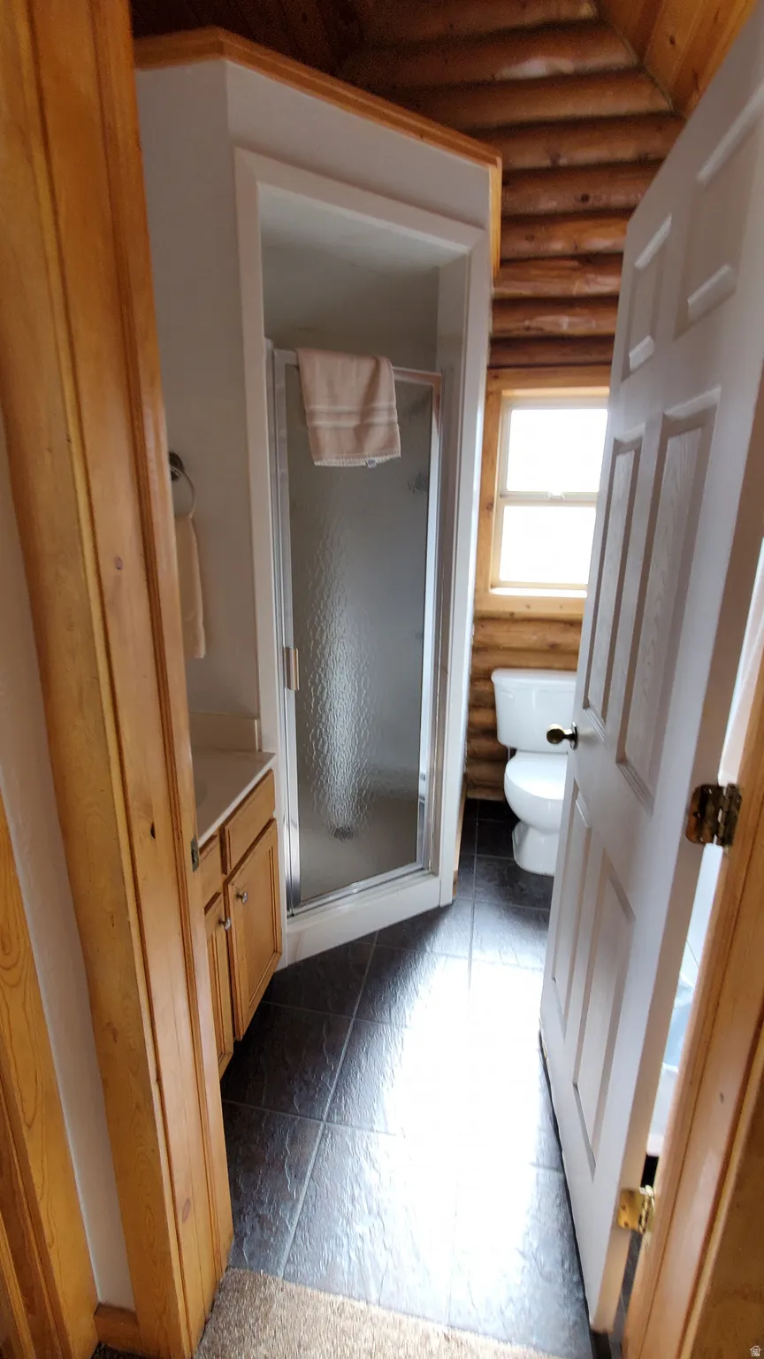 Full bath featuring rustic walls, a stall shower, lofted ceiling, and vanity