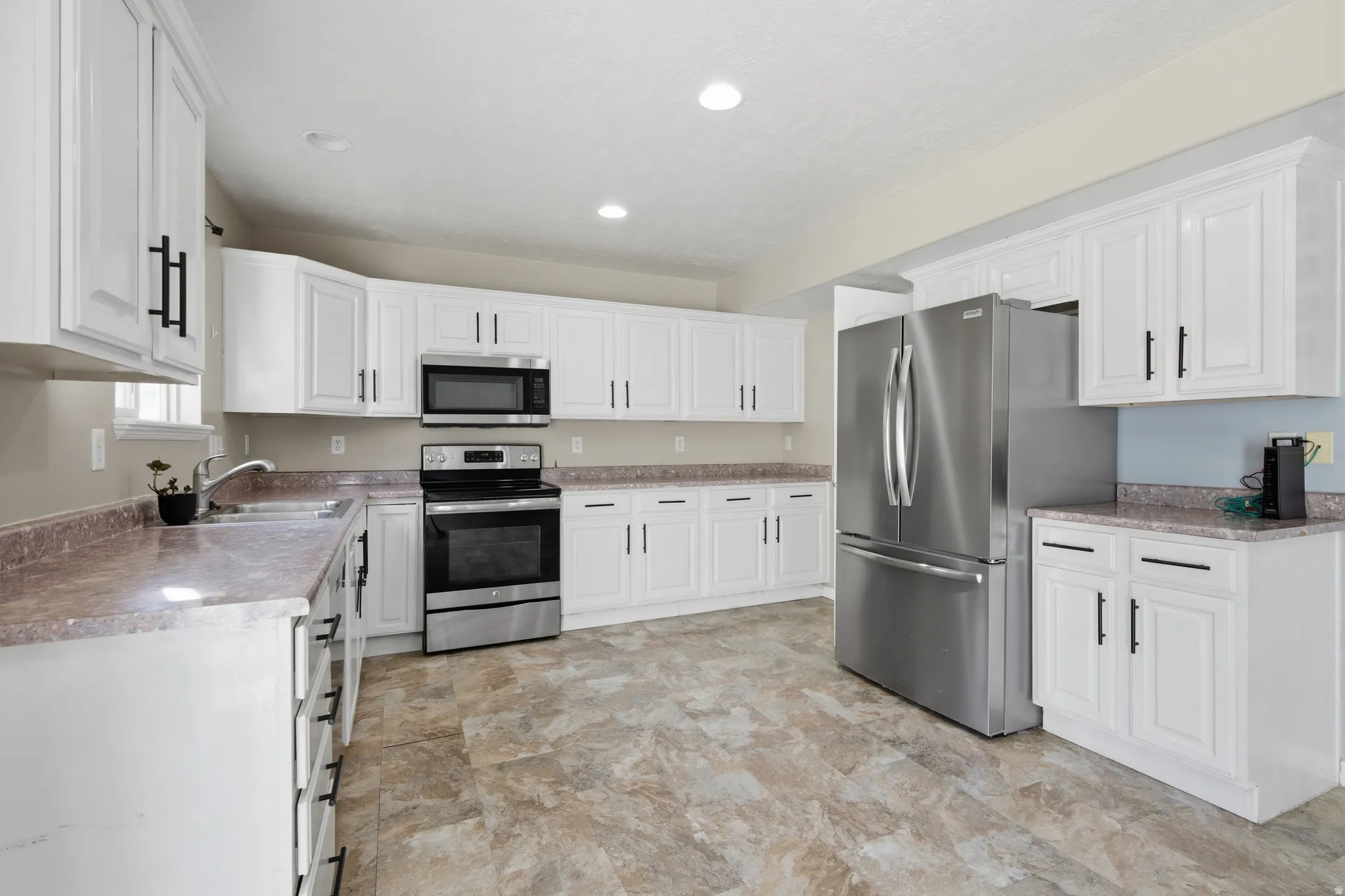 Kitchen with stainless steel appliances, white cabinets, light countertops, recessed lighting