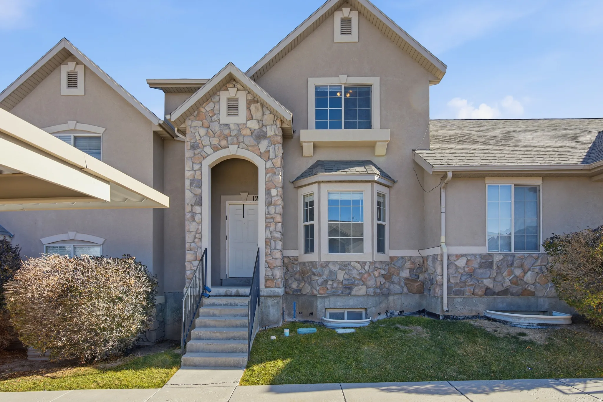 View of front of property with stone siding, stucco siding, a front yard, and a shingled roof