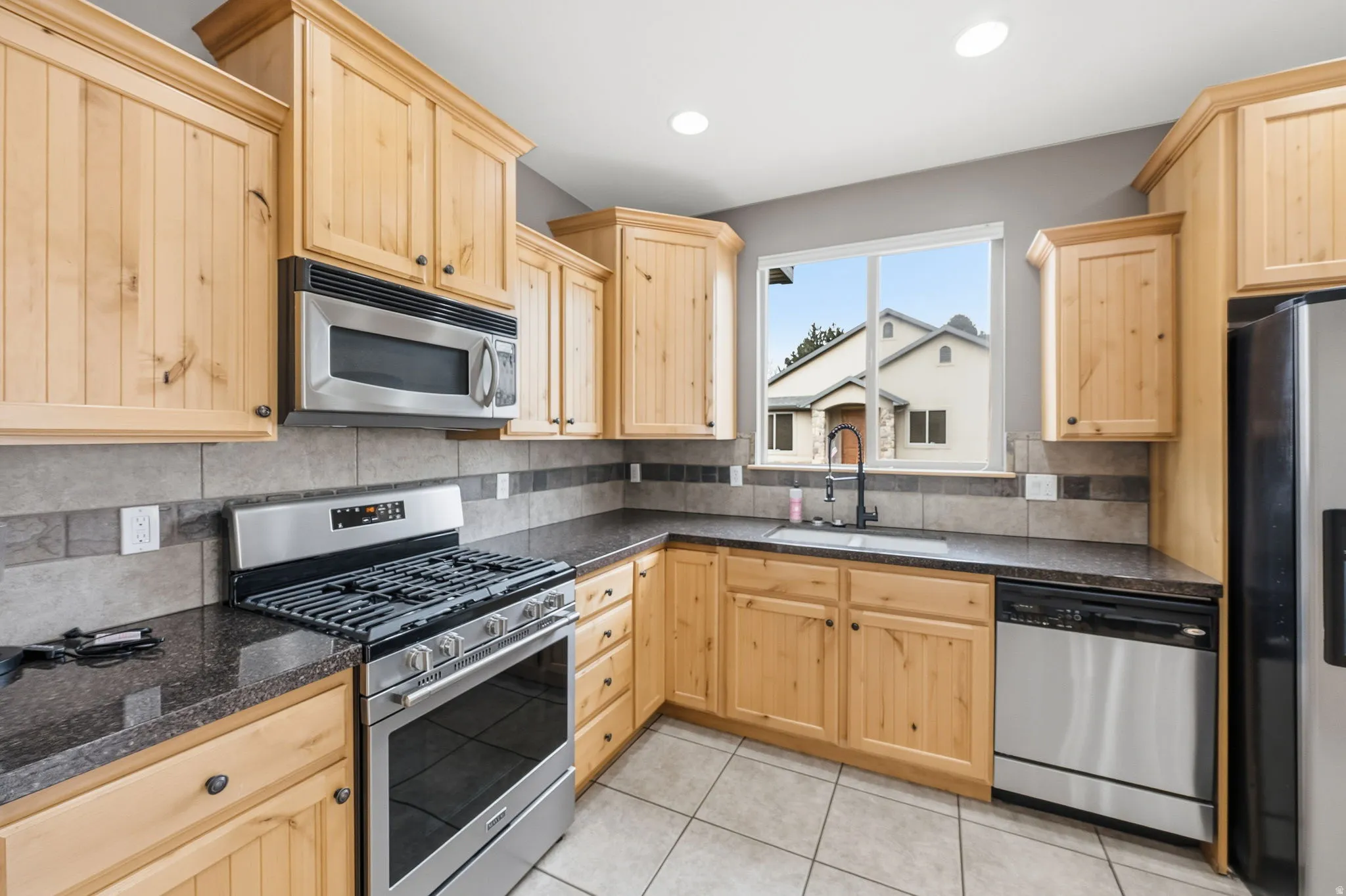 Kitchen with light brown cabinetry, stainless steel appliances, light tile patterned floors, decorative backsplash, and recessed lighting