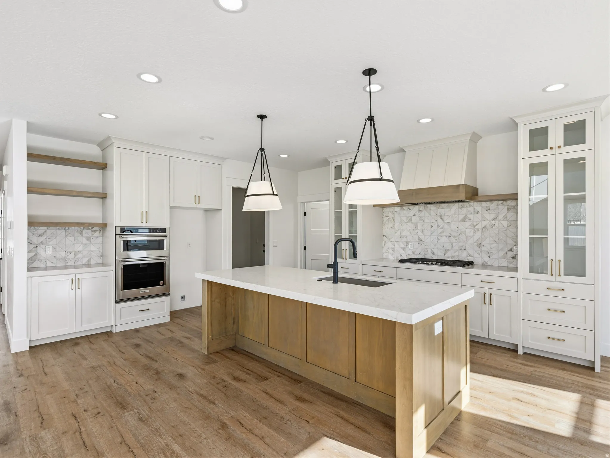 Kitchen featuring open shelves, tasteful backsplash, two tone cabinets, a center island with sink, and stainless steel double oven