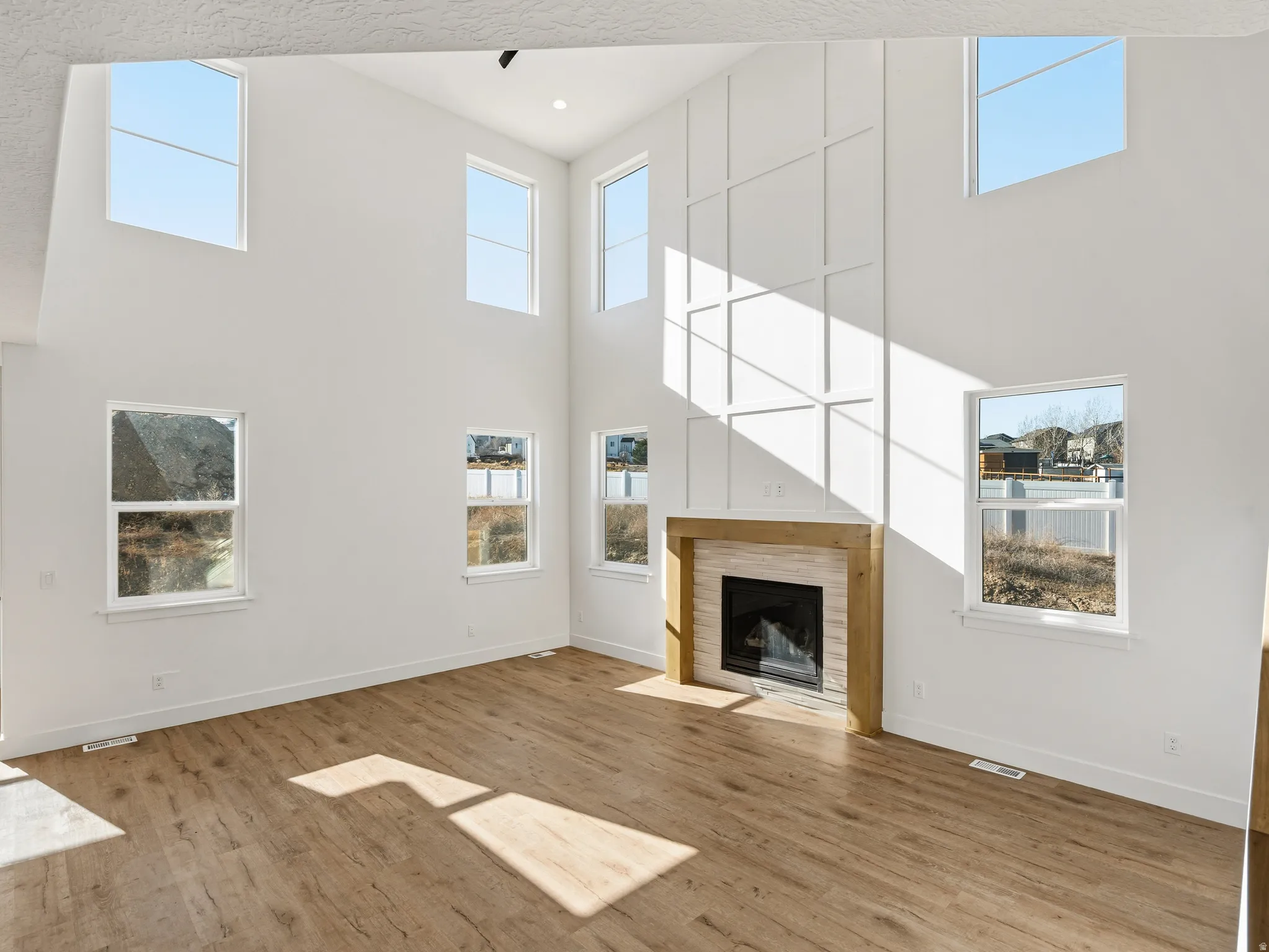 Unfurnished living room with a high ceiling, a tiled fireplace, and wood finished floors