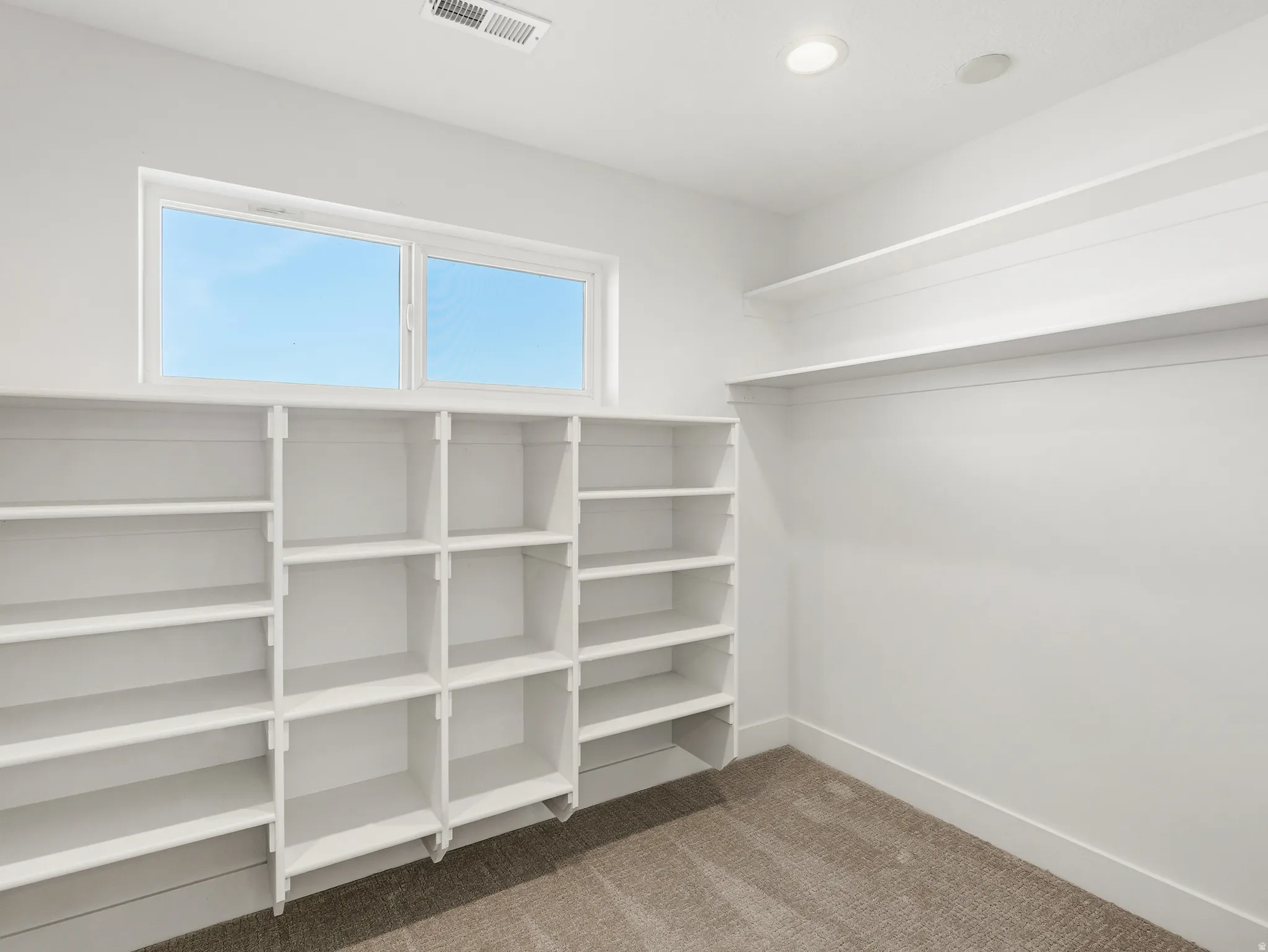 Primary walk in closet featuring light colored carpet