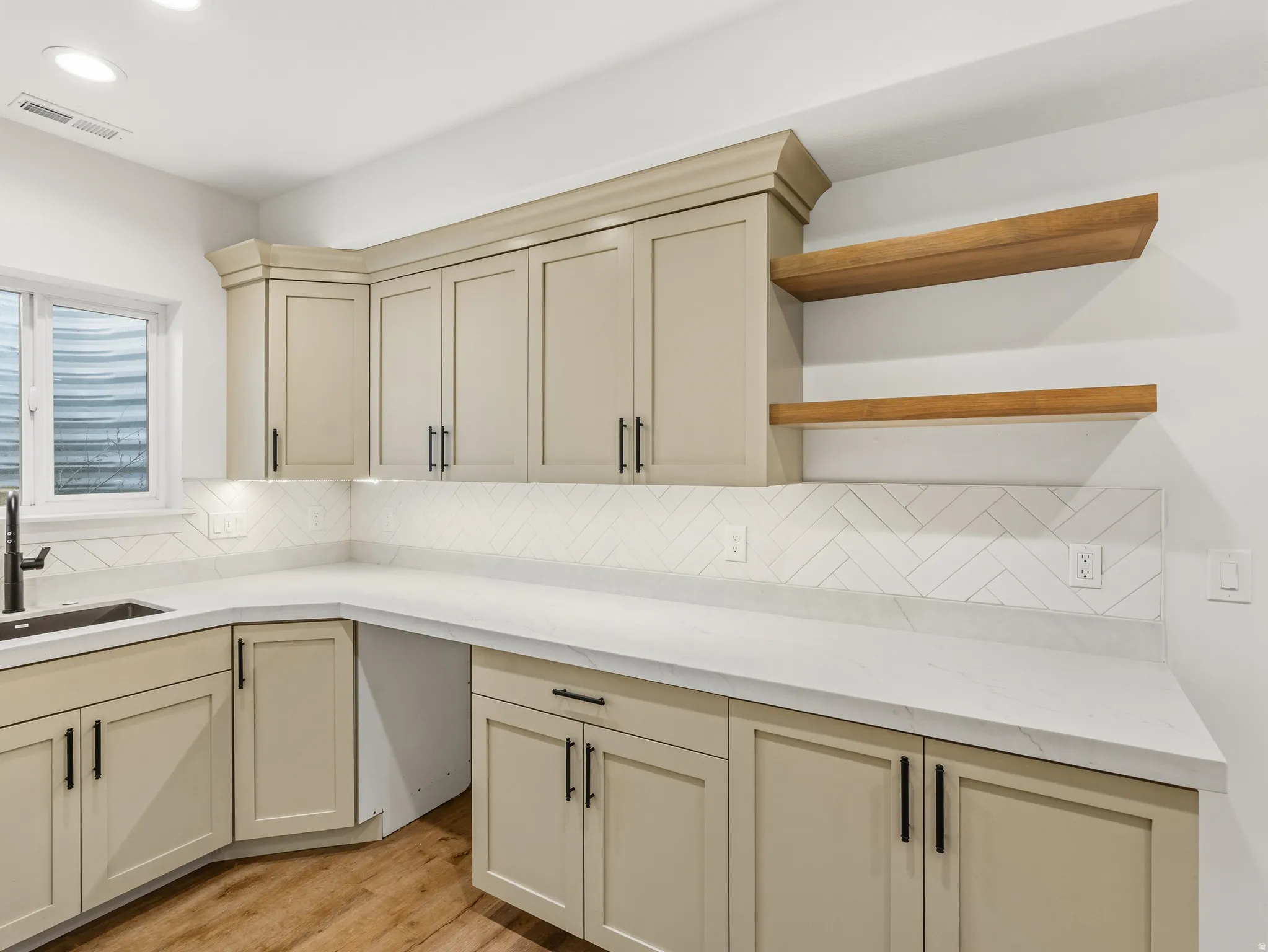 Kitchen featuring cream cabinets, light wood finished floors, light stone counters, backsplash, and recessed lighting