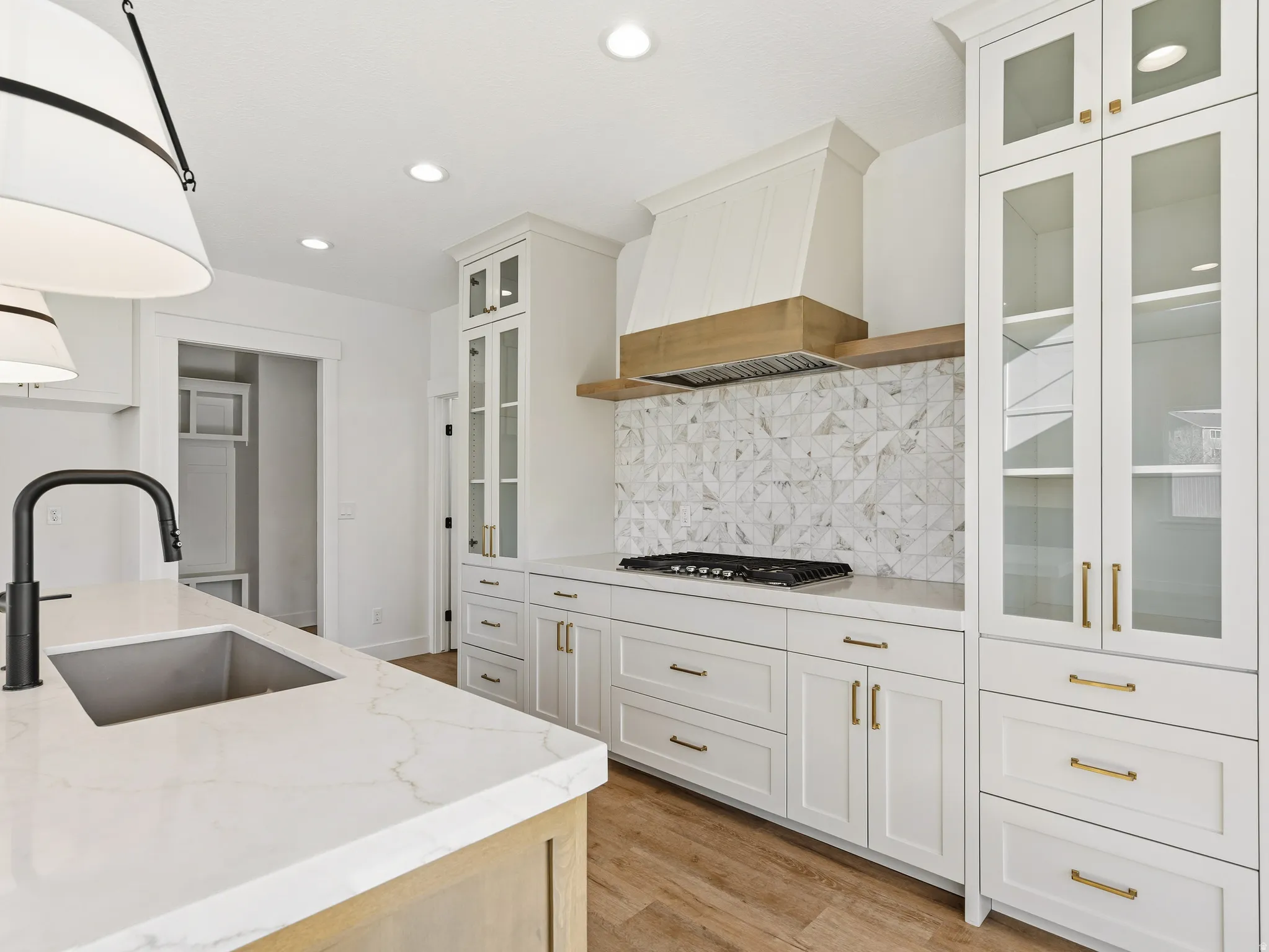 Kitchen featuring glass fronted cabinets, white cabinetry, light stone countertops, and hanging light fixtures