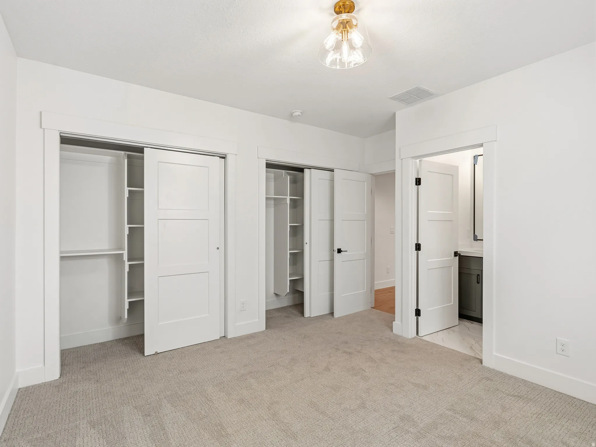 Unfurnished bedroom with multiple closets, light colored carpet, and ensuite bathroom
