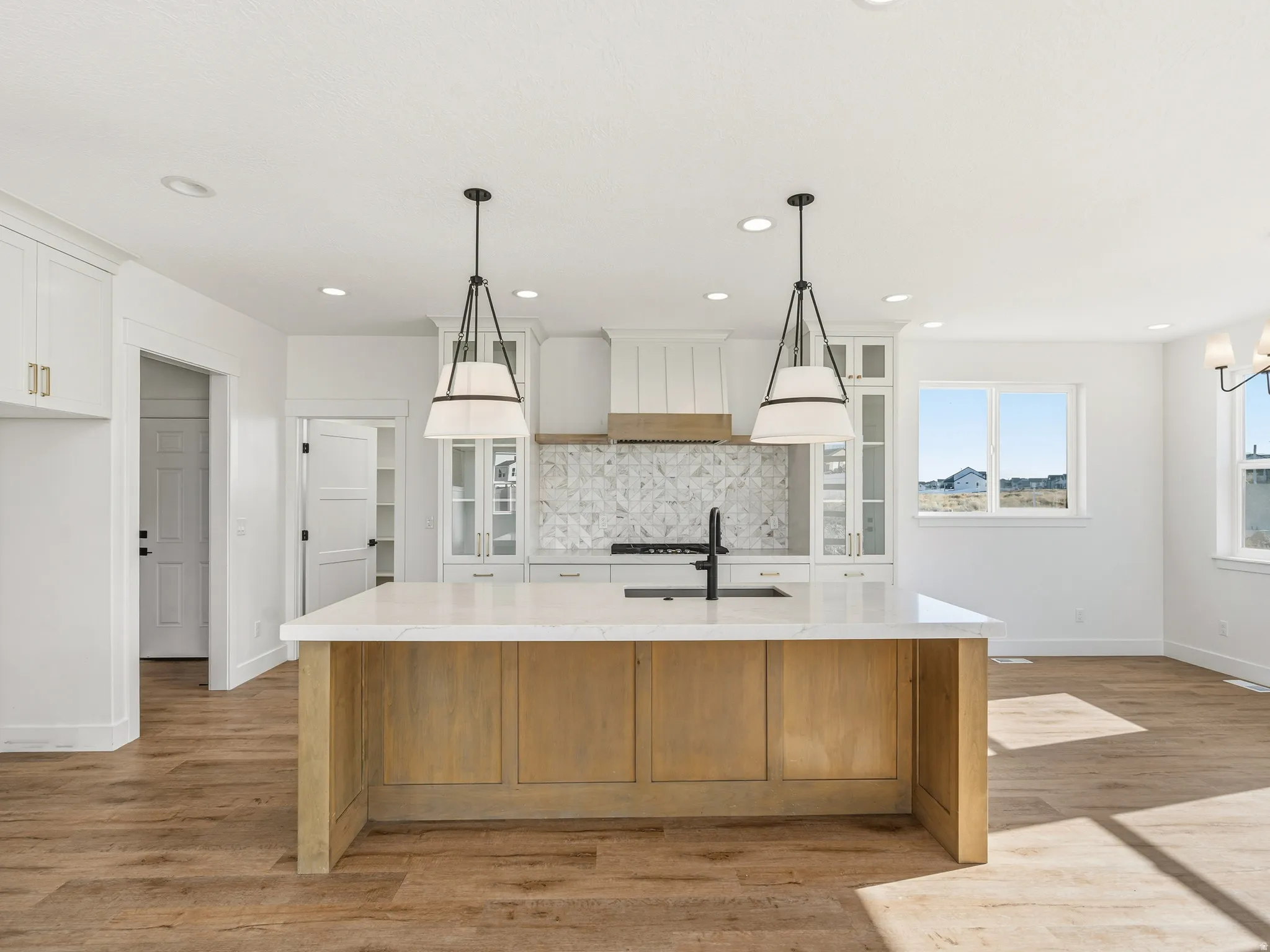 Dual tone kitchen featuring light stone countertops, glass fronted cabinets, a large island with sink, pendant lighting, and two tone color scheme
