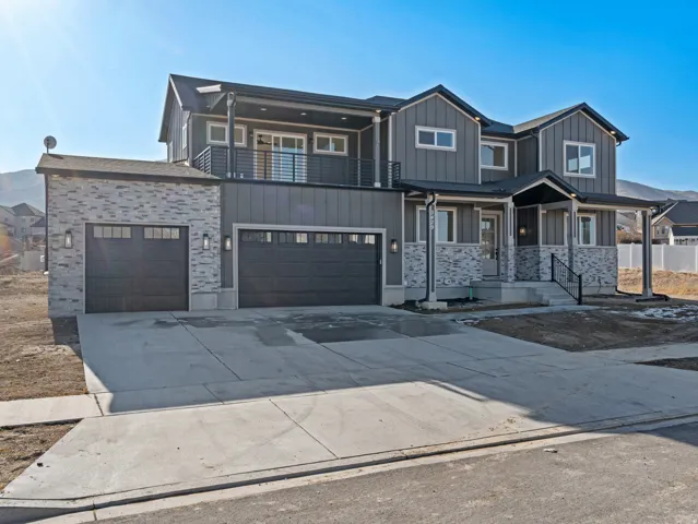 View of front of home featuring board and batten siding, concrete driveway, stone siding, and covered porch