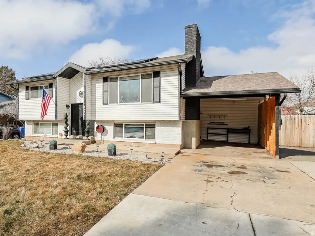Split foyer home with roof mounted solar panels, a front yard, concrete driveway, a chimney, and brick siding