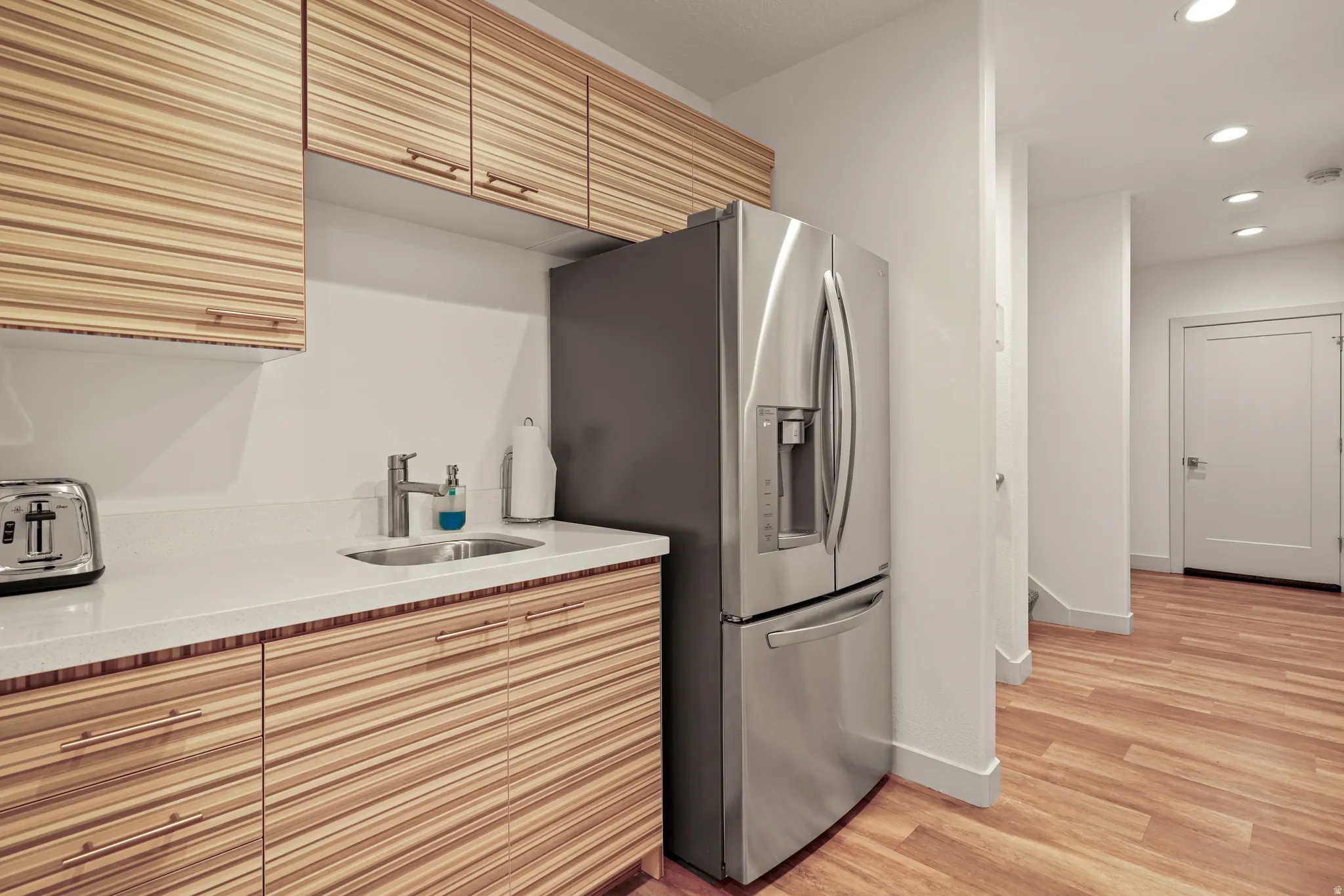 Kitchen featuring stainless steel fridge with ice dispenser, light stone counters, recessed lighting, and light wood finished floors