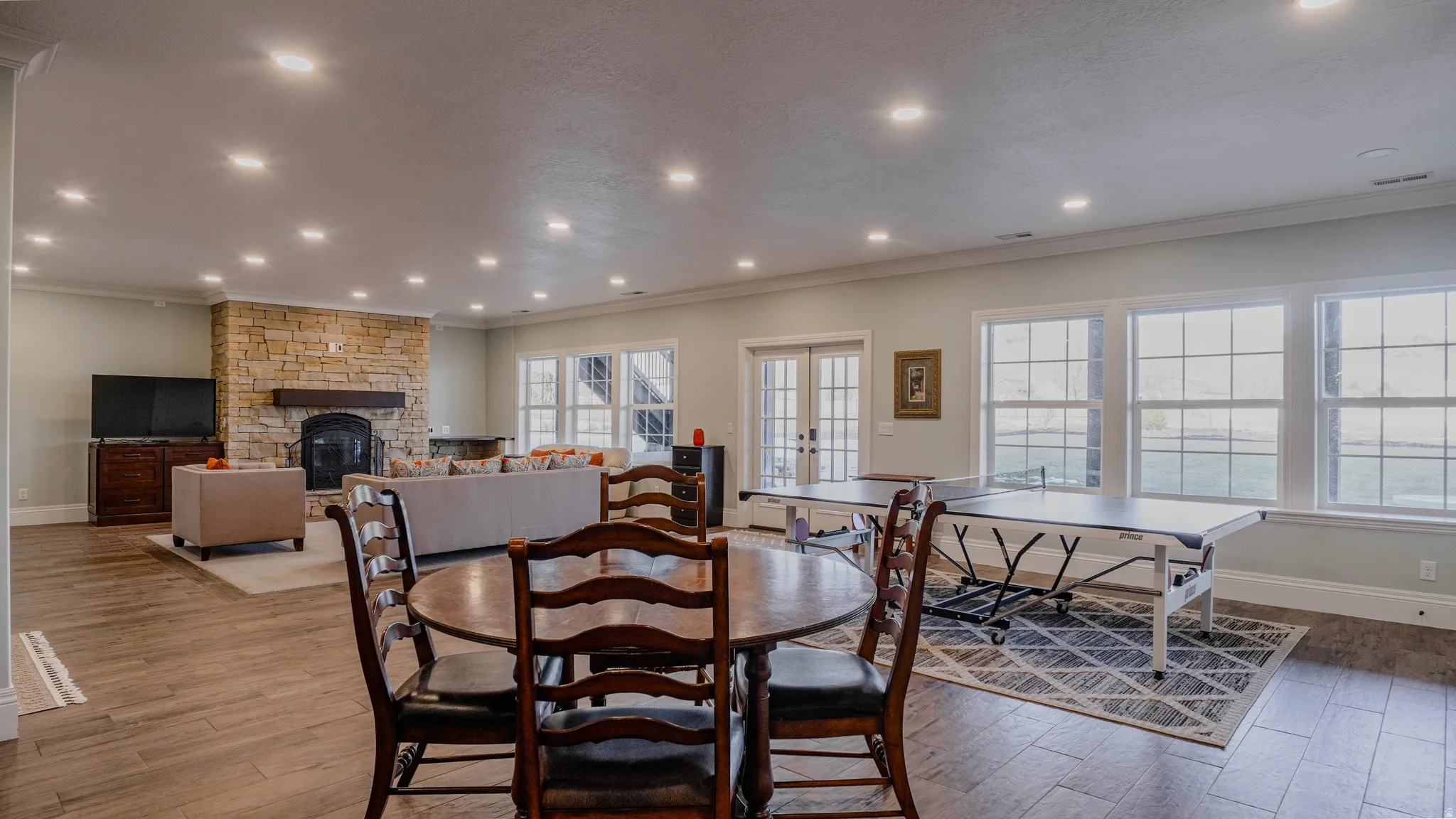 Dining room with light wood-type flooring, recessed lighting, a stone fireplace, ornamental molding, and french doors