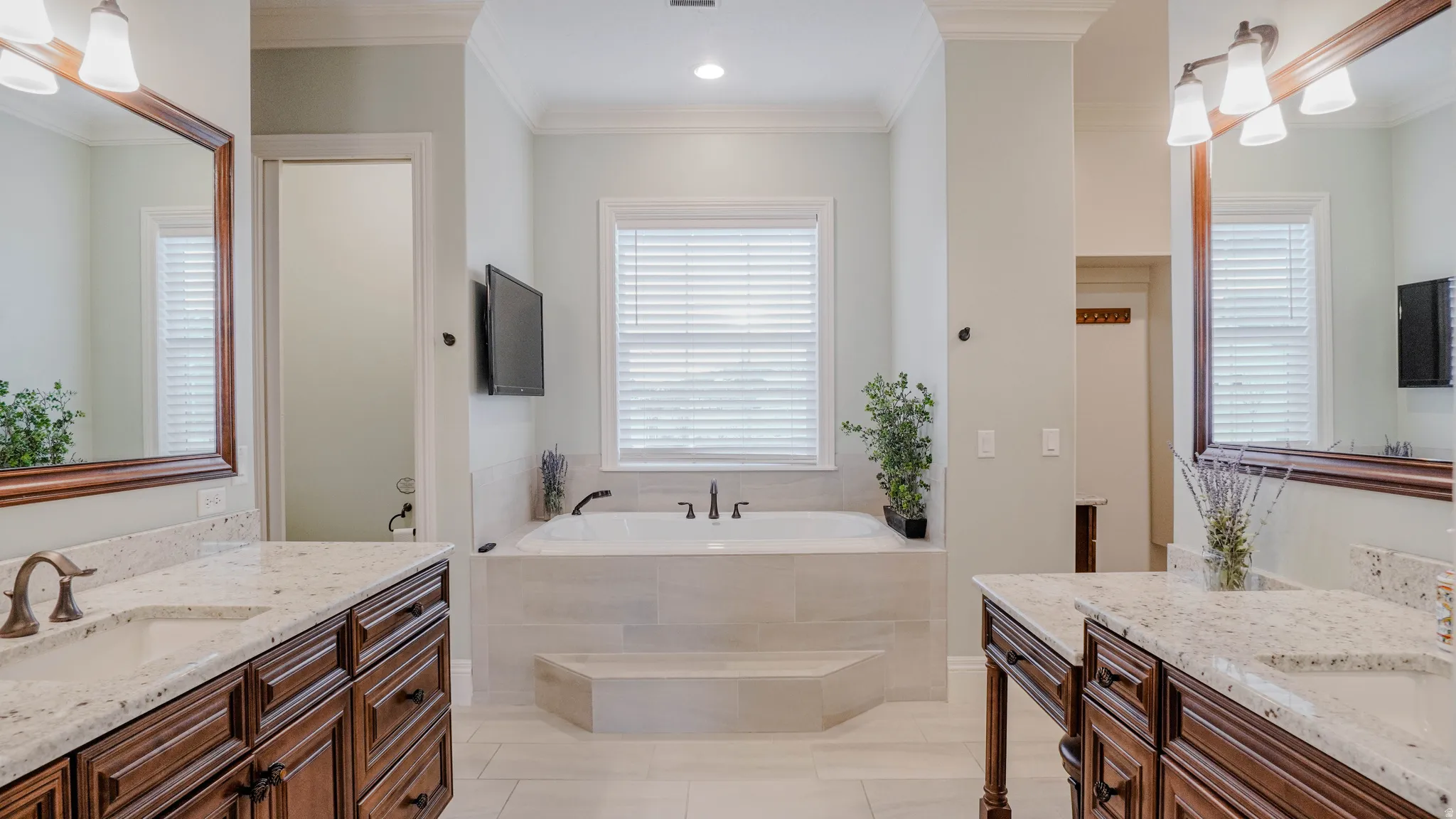 Bathroom featuring ornamental molding, two vanities, a bath, light tile patterned flooring, and plenty of natural light