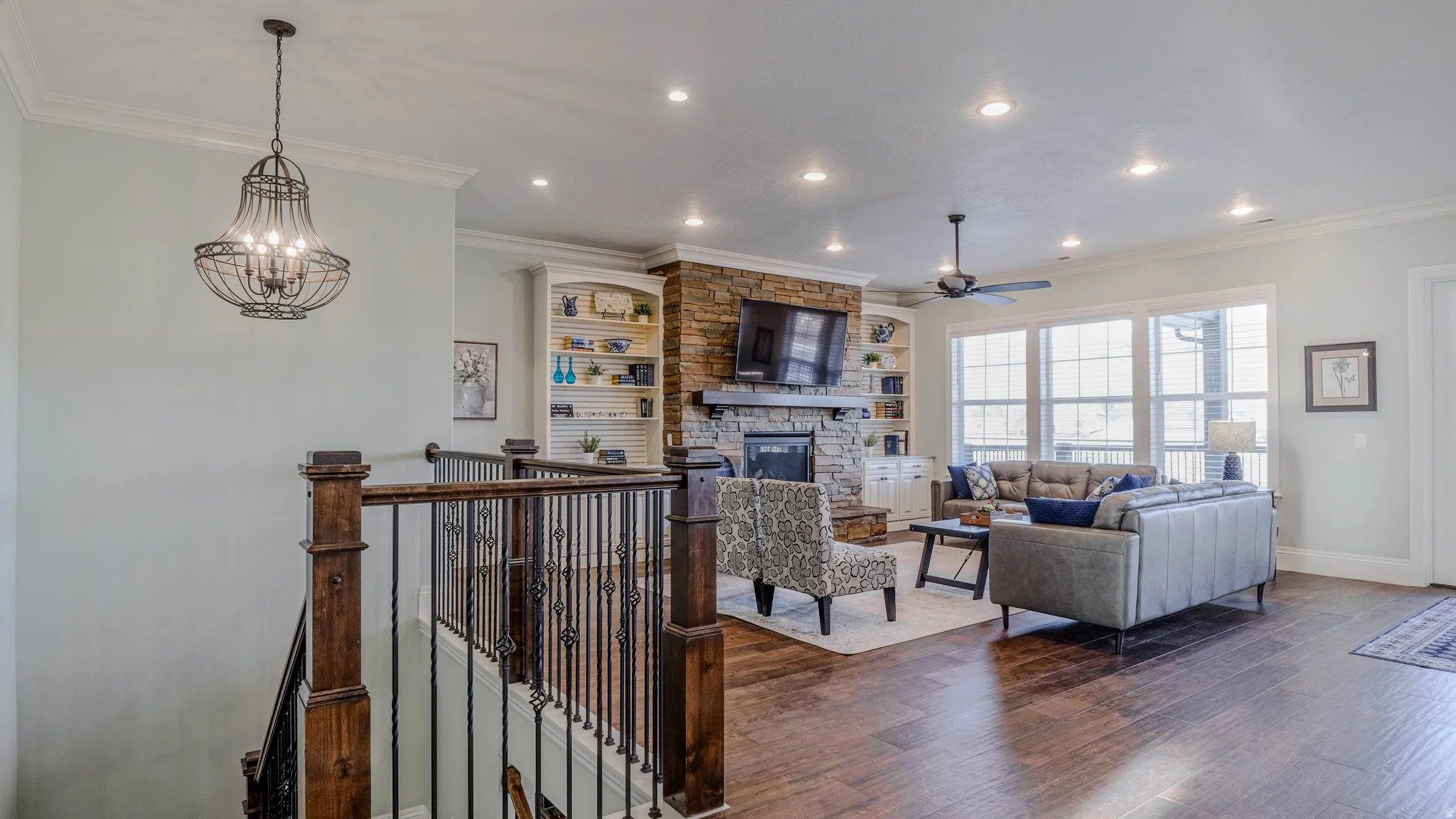 Living area featuring dark wood finished floors, crown molding, recessed lighting, a stone fireplace, and a chandelier