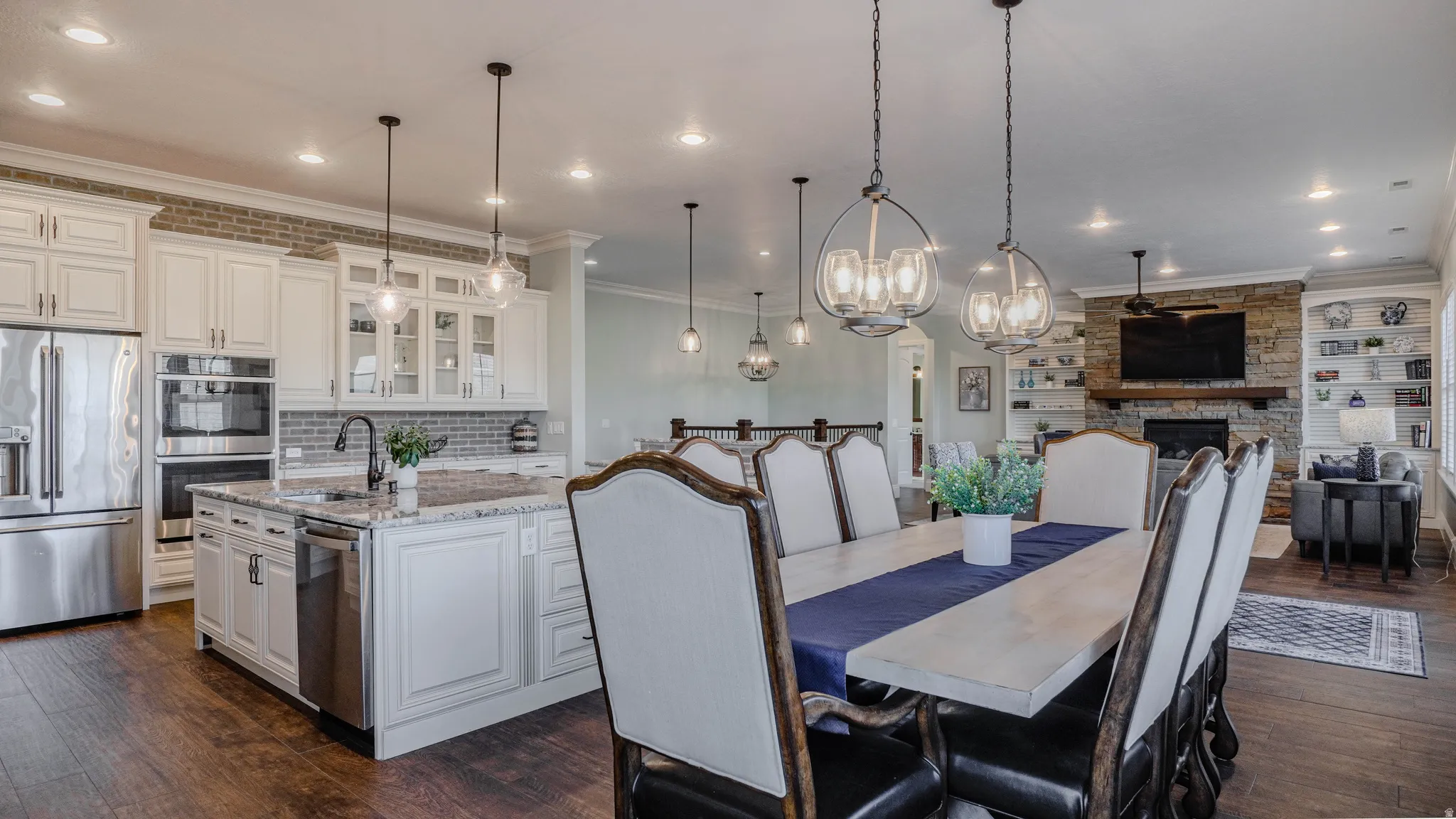 Dining room with dark wood-style floors, a chandelier, a stone fireplace, ornamental molding, and recessed lighting